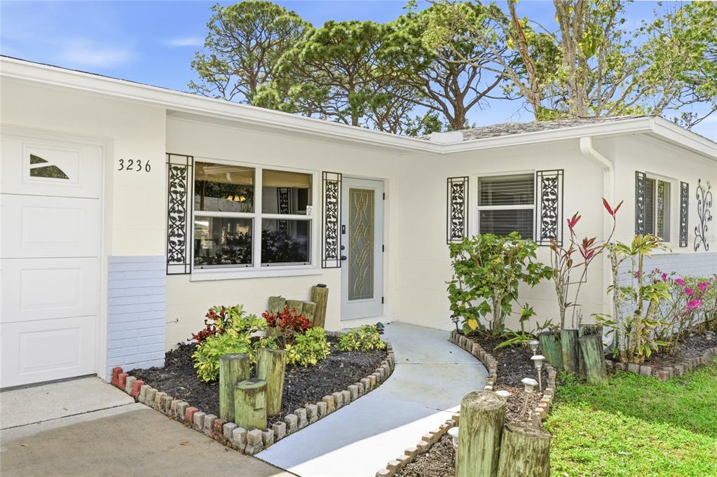 The exterior of a single-story house features white siding, a garage, and a landscaped walkway — 3236 ASHTON ROAD, SARASOTA, FL