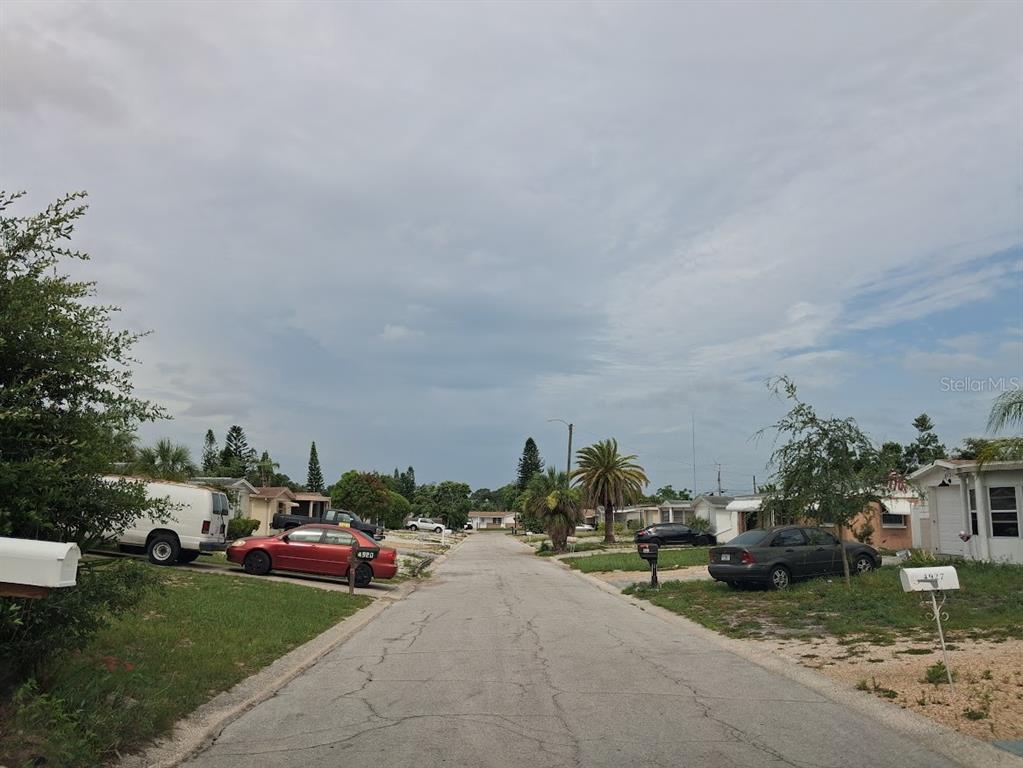 A residential street with parked cars, palm trees, and single-story houses under a cloudy sky — 4926 COLONNADE AVENUE, HOLIDAY, FL
