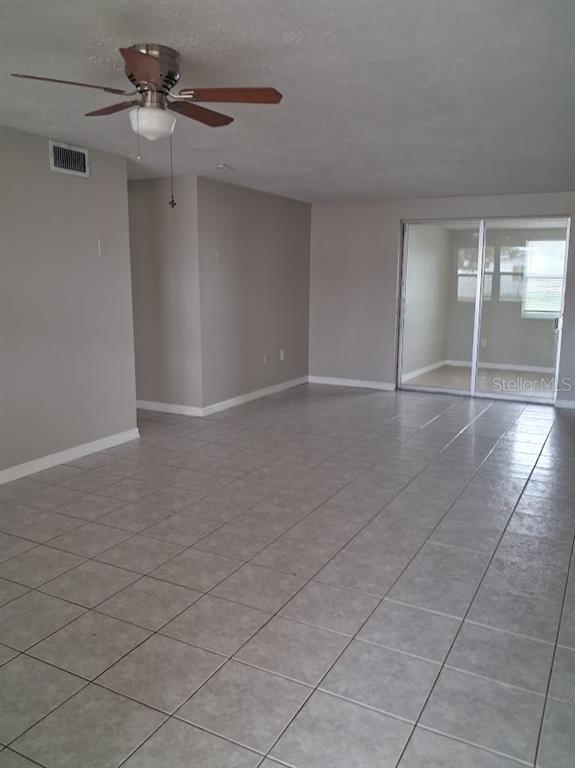 An empty living room features light gray walls, large floor tiles, and a ceiling fan — 4926 COLONNADE AVENUE, HOLIDAY, FL