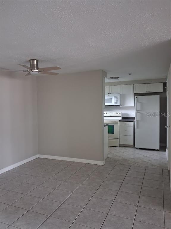 A view of a tiled living area opening into a kitchen with white appliances — 4926 COLONNADE AVENUE, HOLIDAY, FL