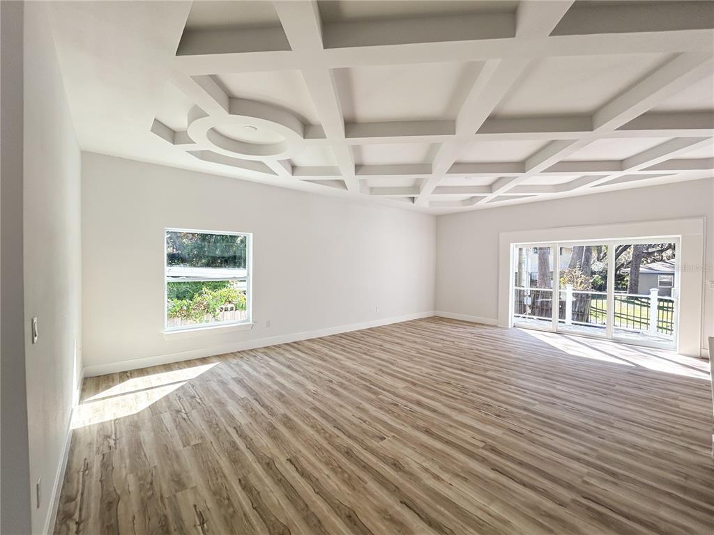 An empty room features light wood-look flooring, white walls, and a decorative coffered ceiling — 407 GEORGIA AVENUE, CRYSTAL BEACH, FL