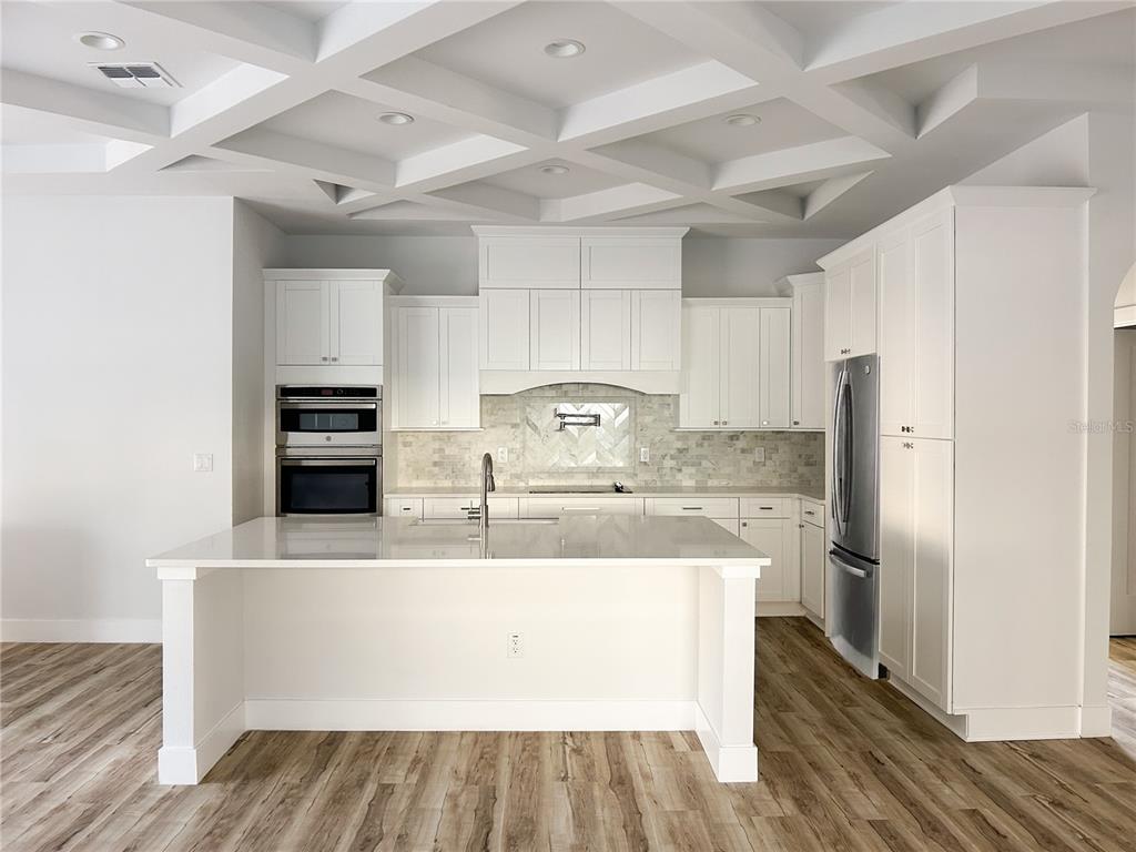 A modern kitchen features white cabinetry, a large center island, and a coffered ceiling — 407 GEORGIA AVENUE, CRYSTAL BEACH, FL