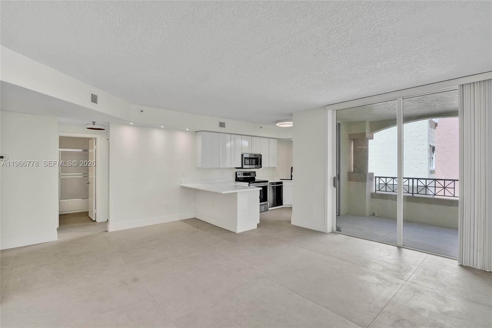 An open-concept kitchen with white cabinetry and tile flooring connects to a balcony through glass doors — 1834 Brickell Ave # 31, Miami FL 33129, MIAMI, FL