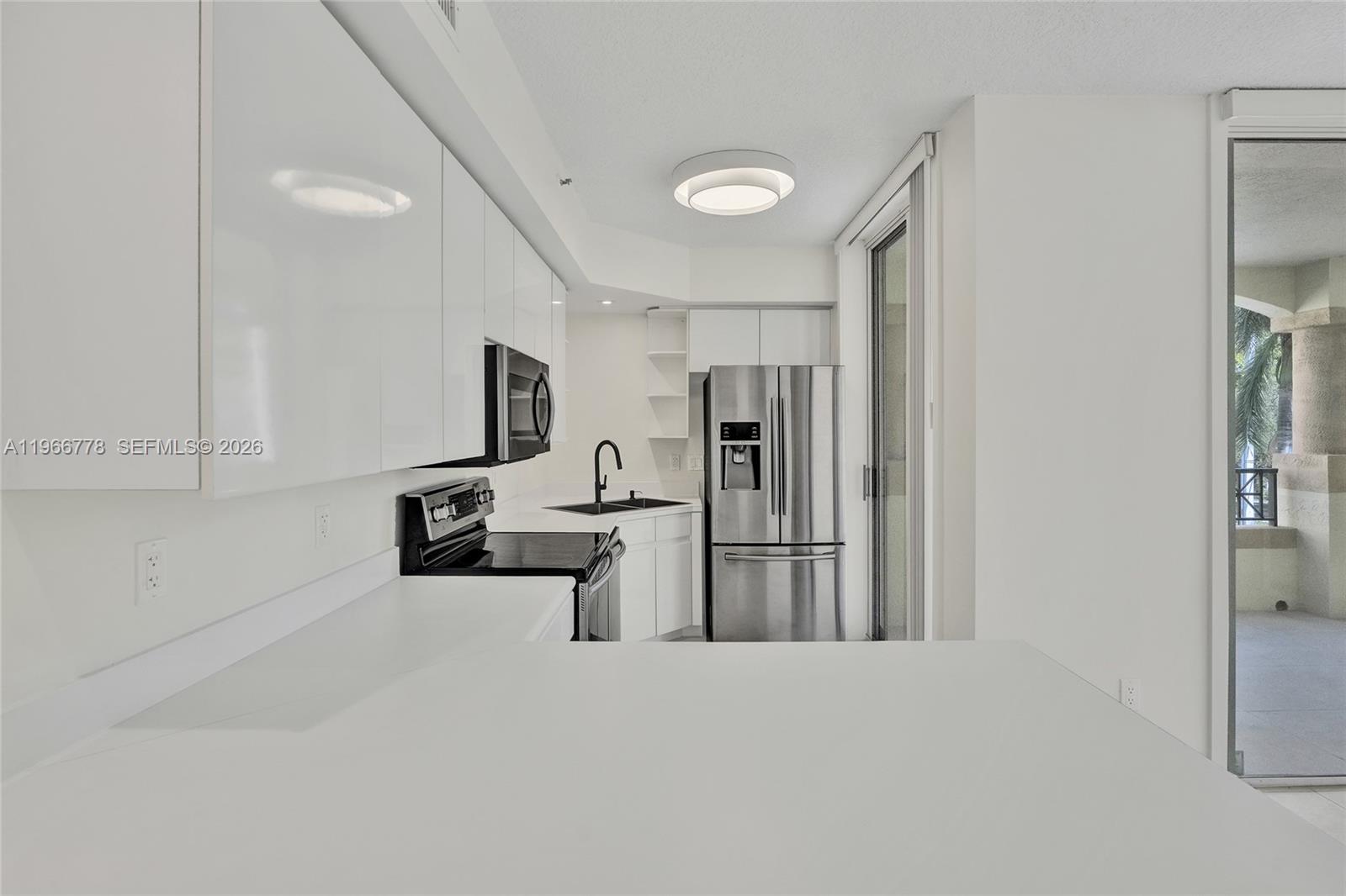 A modern kitchen features white cabinetry, stainless steel appliances, and a view of a balcony — 1834 Brickell Ave # 31, Miami FL 33129, MIAMI, FL