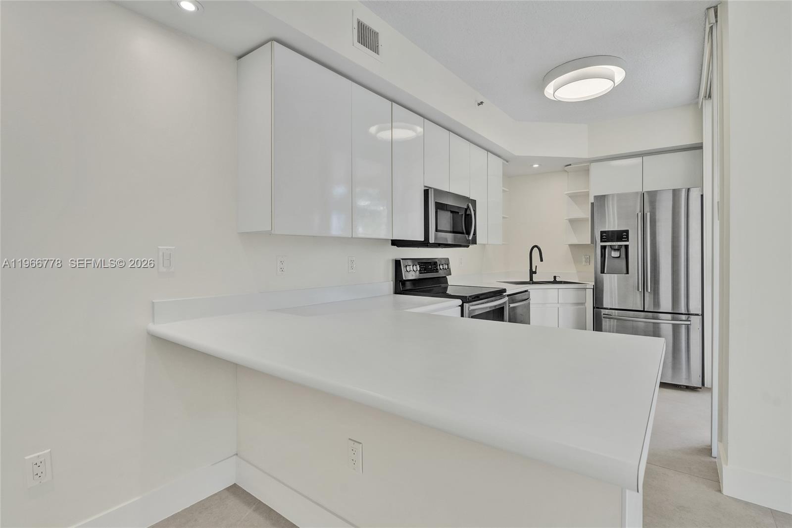 A modern kitchen features white cabinets, stainless steel appliances, and a white countertop peninsula — 1834 Brickell Ave # 31, Miami FL 33129, MIAMI, FL