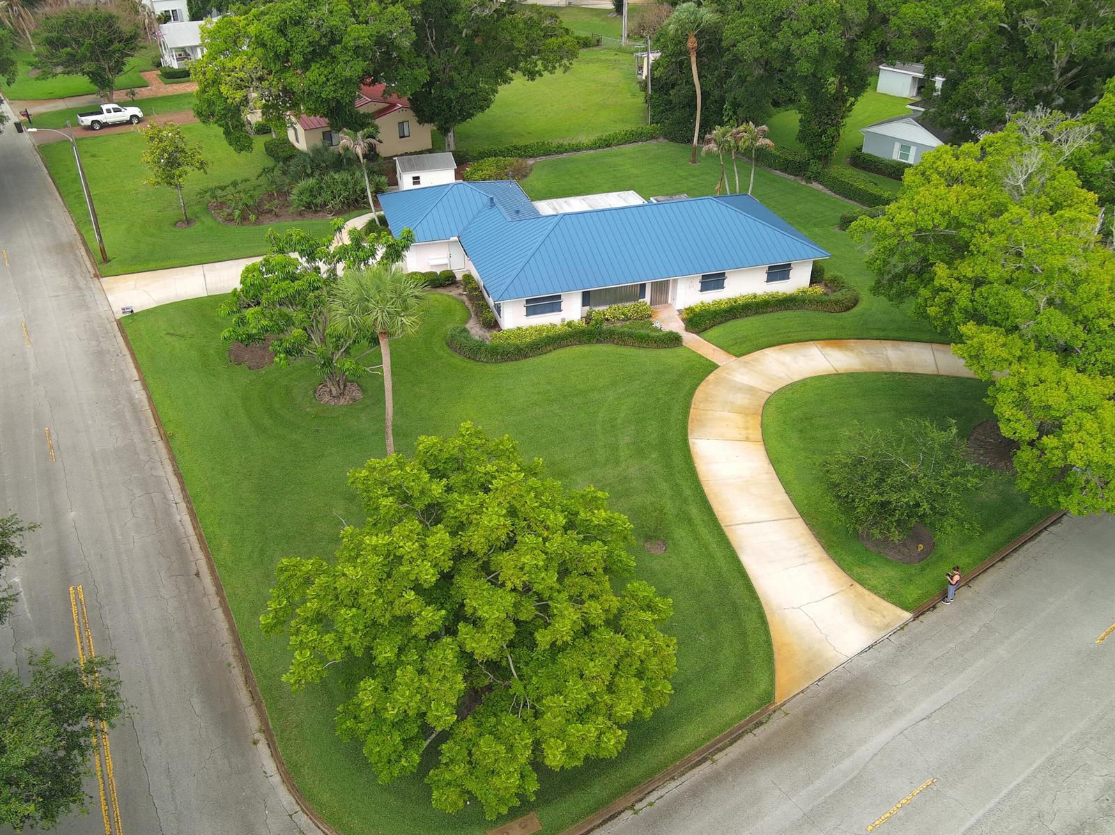 An aerial view shows a white house with a blue metal roof and curved driveway — 2301 Avalon Avenue, Vero Beach FL 32960, VERO BEACH, FL