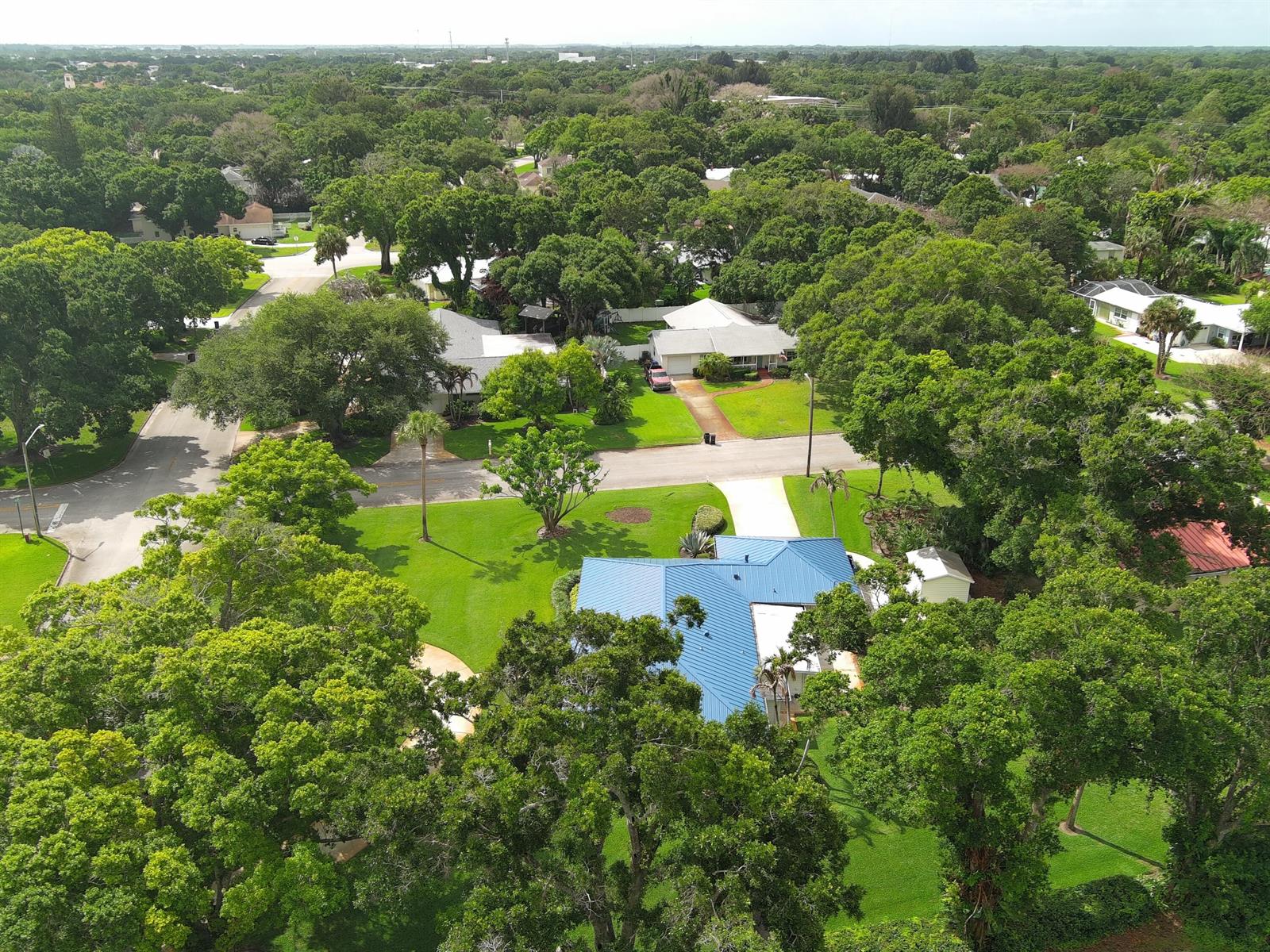 An aerial view shows a house with a blue metal roof surrounded by many trees — 2301 Avalon Avenue, Vero Beach FL 32960, VERO BEACH, FL