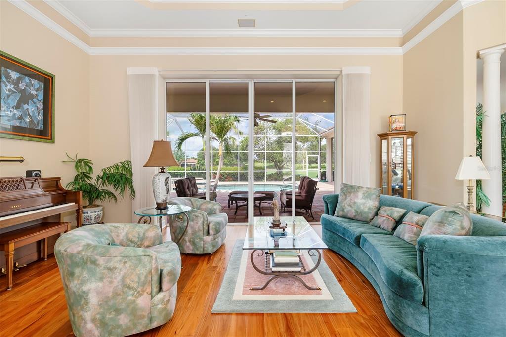 A living room features a teal sofa, patterned armchairs, a piano, and sliding glass doors — 2528 TOM MORRIS DRIVE, SARASOTA, FL