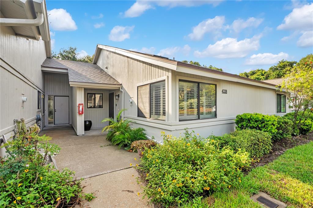 The exterior of a light-colored house features a concrete walkway, landscaping, and large windows — 4338 SEA MIST DRIVE, NEW SMYRNA BEACH, FL