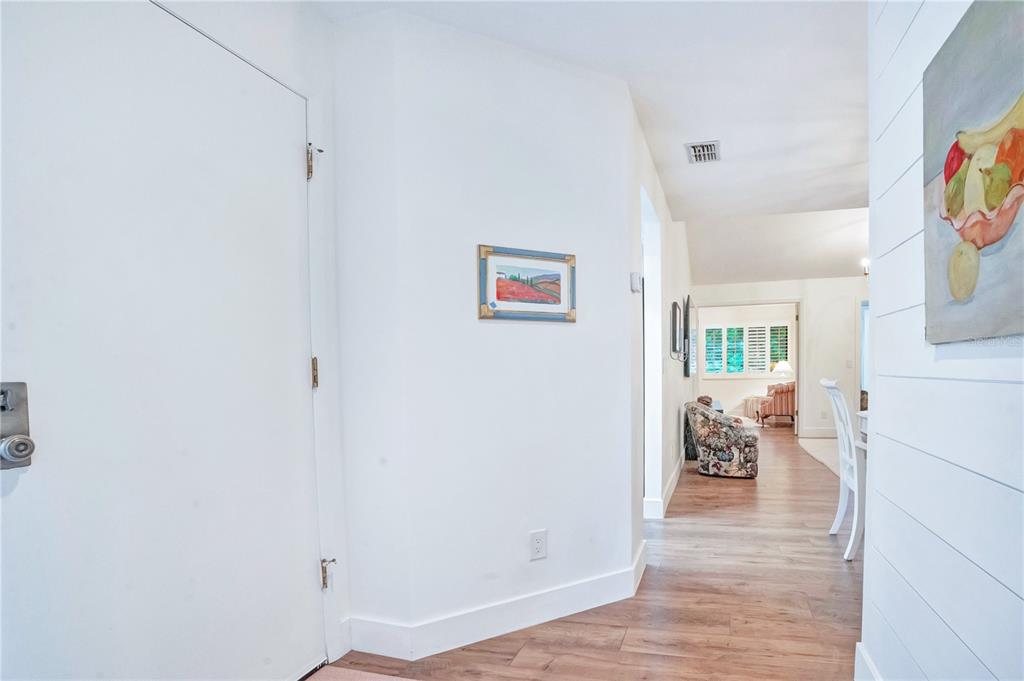 A white hallway leads to a living area with wood-look flooring and wall art — 4338 SEA MIST DRIVE, NEW SMYRNA BEACH, FL