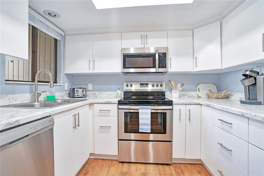 A kitchen features white cabinets, stainless steel appliances, and marble-patterned countertops over wood-look flooring — 4338 SEA MIST DRIVE, NEW SMYRNA BEACH, FL