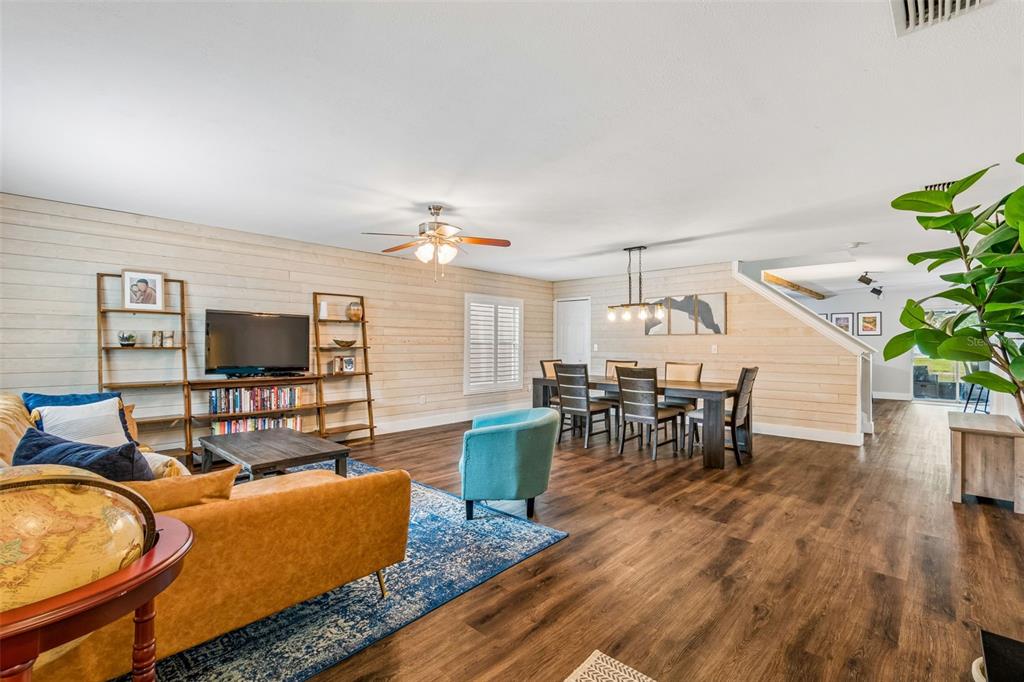 A living and dining room features wood-plank walls, dark flooring, and a blue area rug — 13715 TRAMORE DRIVE, ODESSA, FL