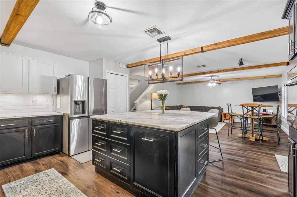 A kitchen with a large black island, marble countertop, and wood ceiling beams — 13715 TRAMORE DRIVE, ODESSA, FL