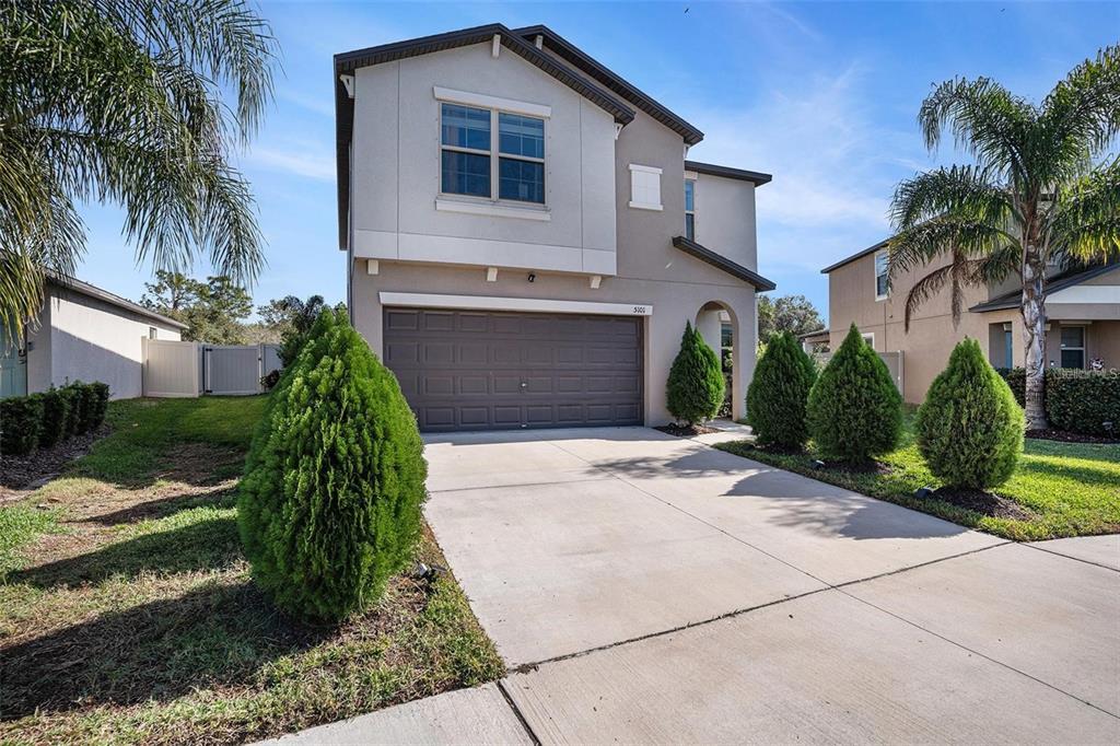 A two-story suburban house with a concrete driveway, a garage, and several manicured shrubs — 5101 SABLE CHIME DRIVE, WIMAUMA, FL