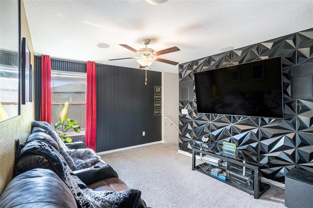 A home theater room features a large wall-mounted television, textured black wall panels, and leather seating — 5101 SABLE CHIME DRIVE, WIMAUMA, FL