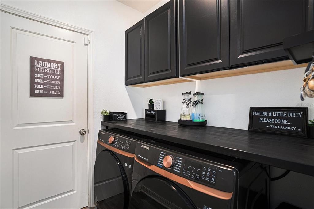 A laundry room features black cabinets, a dark wood countertop, and matching Samsung appliances — 5101 SABLE CHIME DRIVE, WIMAUMA, FL