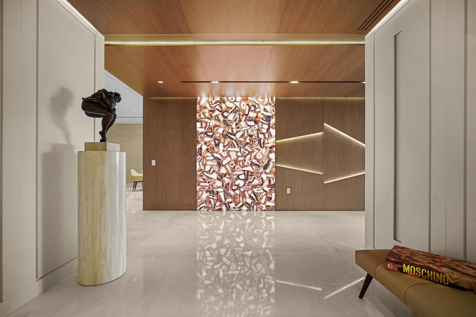 A modern entryway features a stone sculpture, a backlit agate wall, and wood-paneled walls — 725 S Ocean Boulevard # 206, Boca Raton FL 33432, BOCA RATON, FL