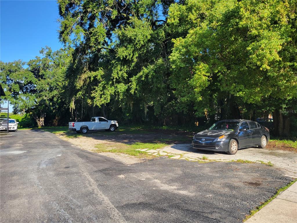 A gravel and asphalt parking area sits beneath large trees next to two parked cars — 424 SUNSET DRIVE, ORLANDO, FL