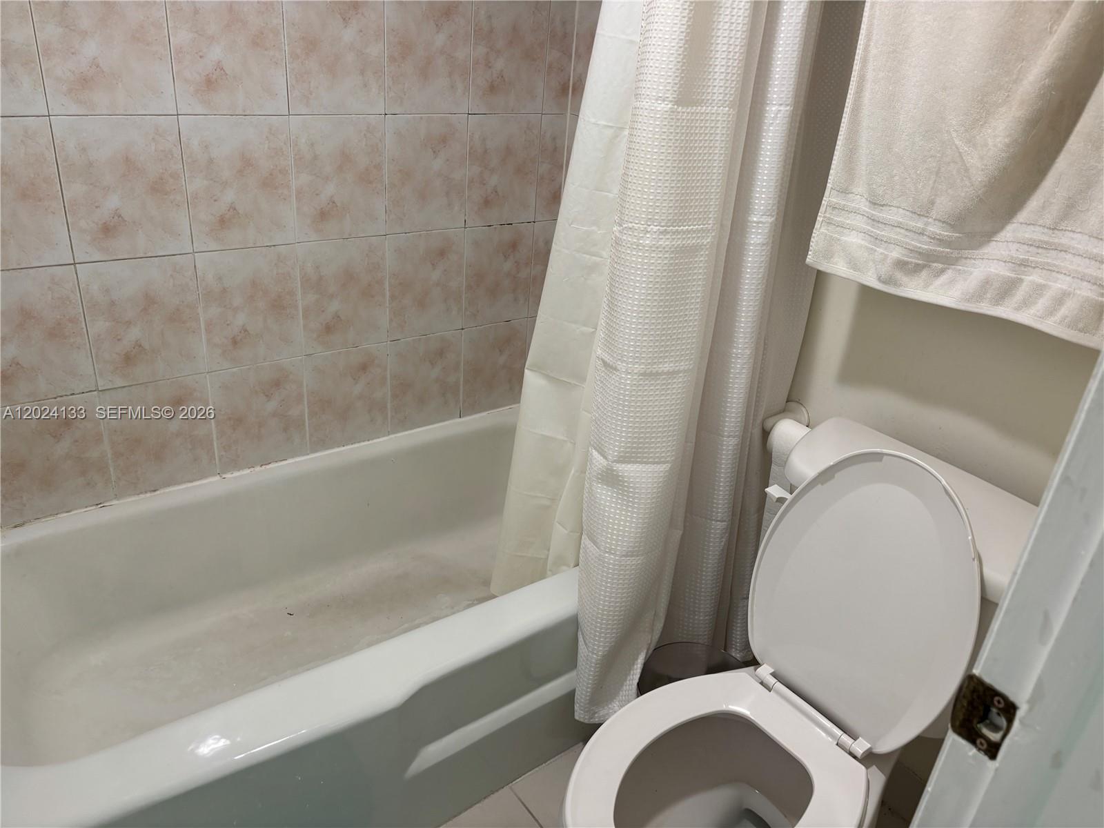A white bathtub with a shower curtain sits next to a toilet in a bathroom — 10806 N Kendall Dr # 26, Miami FL 33176, MIAMI, FL
