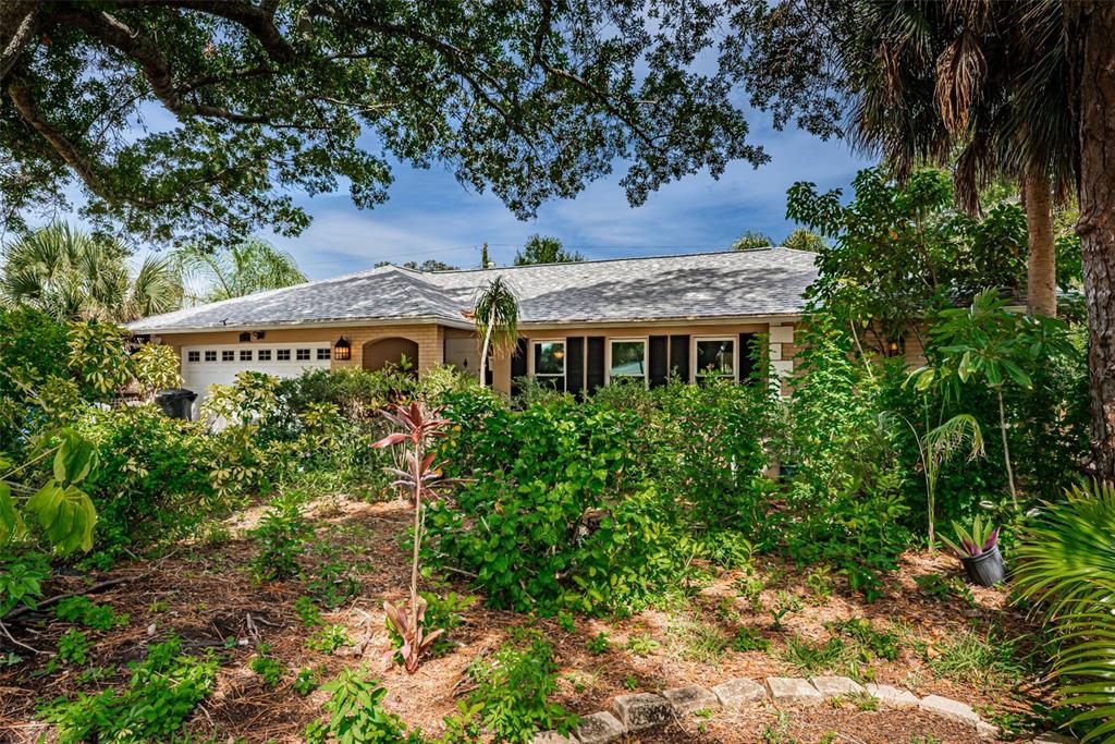 A single-story house with a light-colored brick exterior is partially obscured by dense front landscaping — 5230 VENETIAN BOULEVARD NE, ST PETERSBURG, FL
