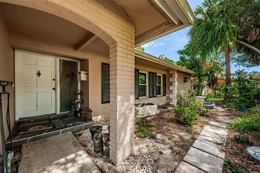 A tan brick house exterior features a front porch, white door, and stone walkway — 5230 VENETIAN BOULEVARD NE, ST PETERSBURG, FL
