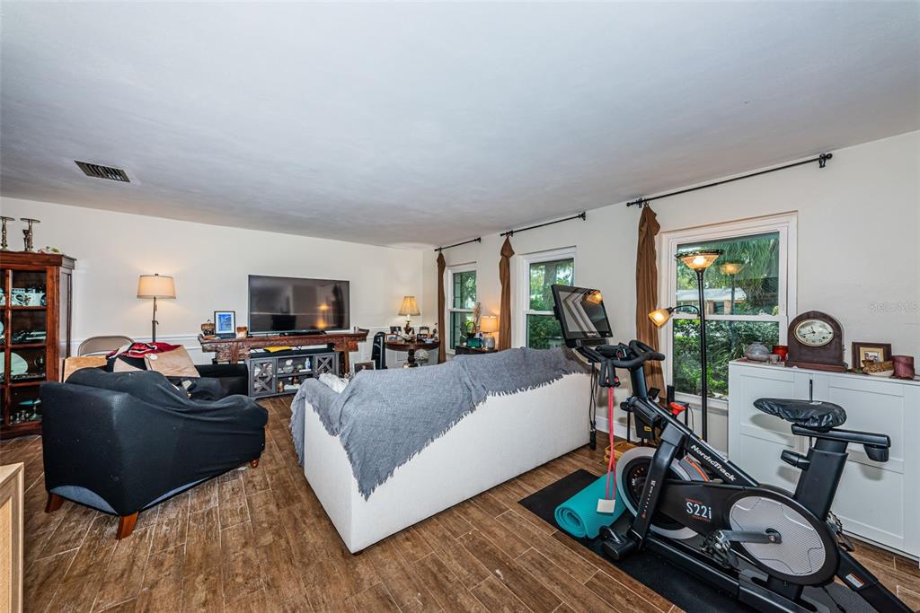 A living room features wood-look tile flooring, a white sofa, a black armchair, and an exercise bike — 5230 VENETIAN BOULEVARD NE, ST PETERSBURG, FL