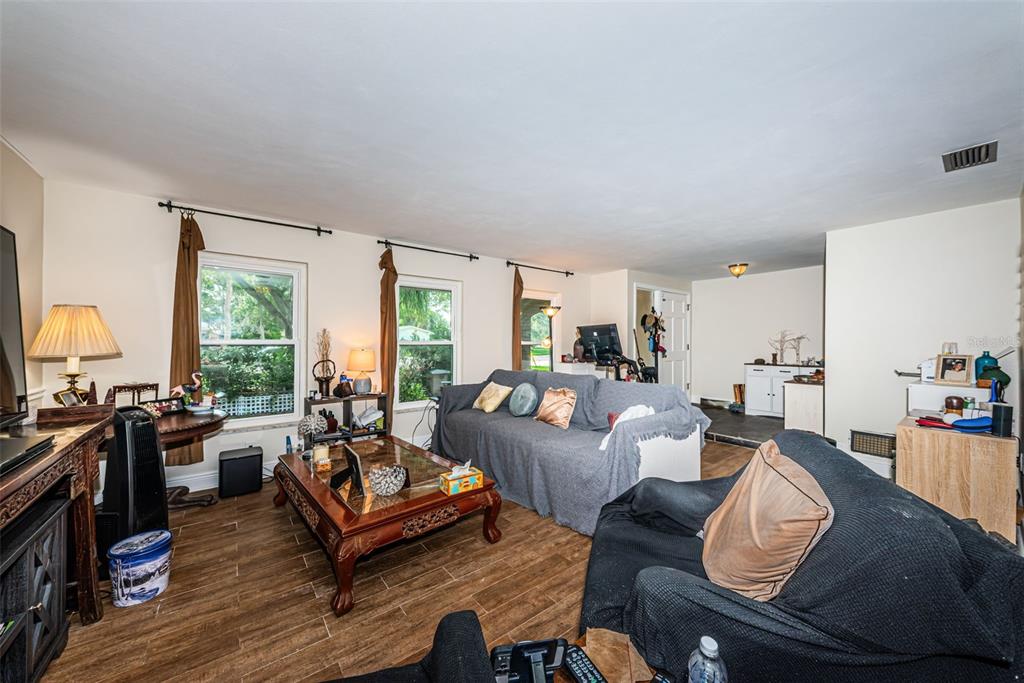 A living room with wood-look tile flooring, two sofas, and three windows with brown curtains — 5230 VENETIAN BOULEVARD NE, ST PETERSBURG, FL