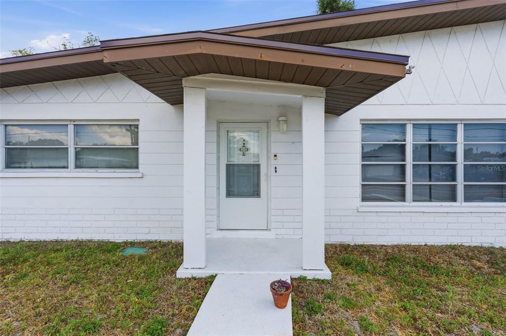 A white house exterior features a covered entryway with a concrete walkway and brown trim — 11830 86TH AVENUE, SEMINOLE, FL