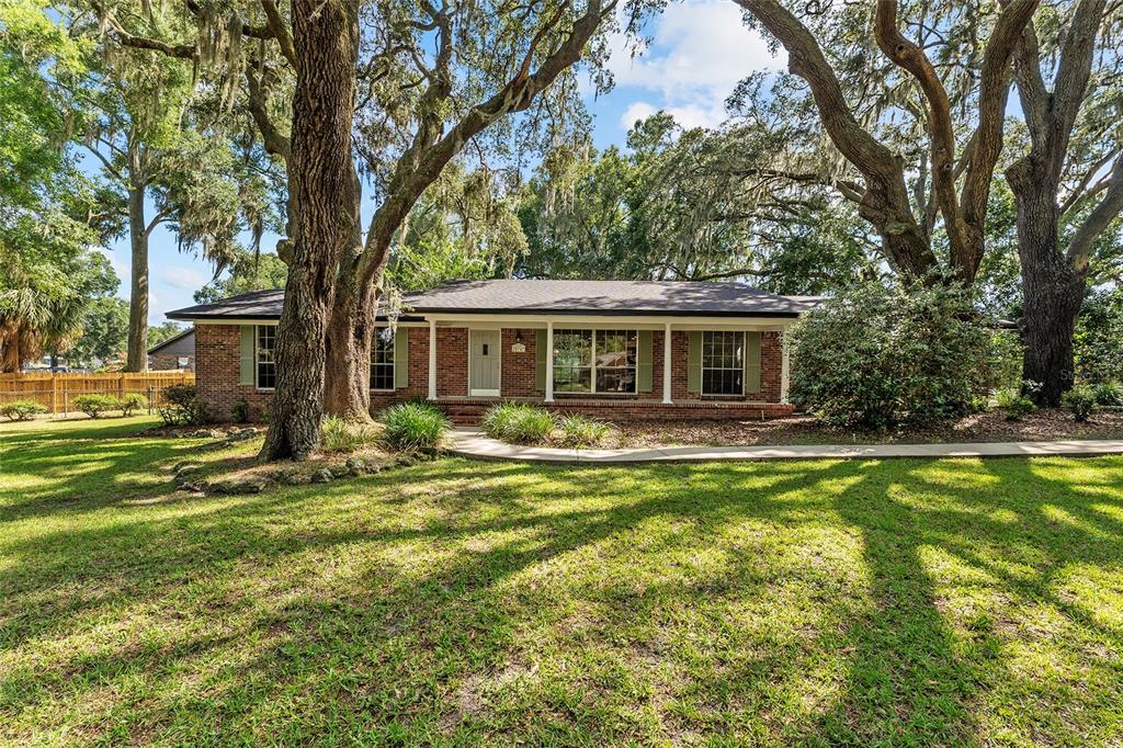 A single-story brick house with a front porch sits on a lawn under large trees — 25747 SW 19TH AVENUE, NEWBERRY, FL