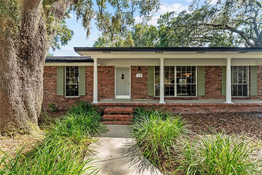 A brick ranch-style house features a covered front porch, white columns, and green shutters — 25747 SW 19TH AVENUE, NEWBERRY, FL