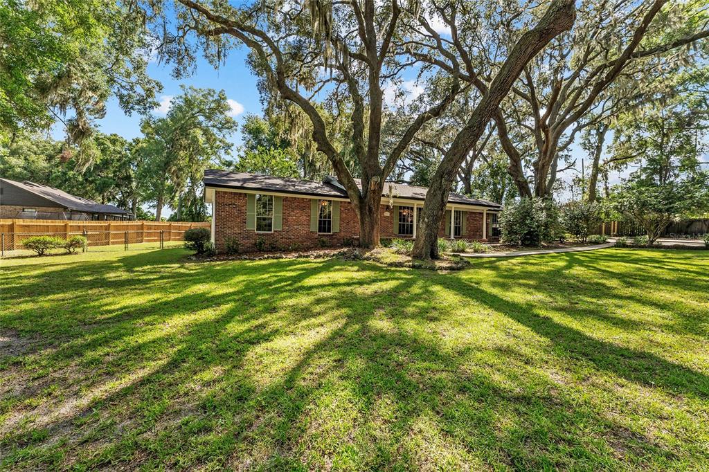 A single-story brick house sits on a grassy lawn shaded by large oak trees — 25747 SW 19TH AVENUE, NEWBERRY, FL