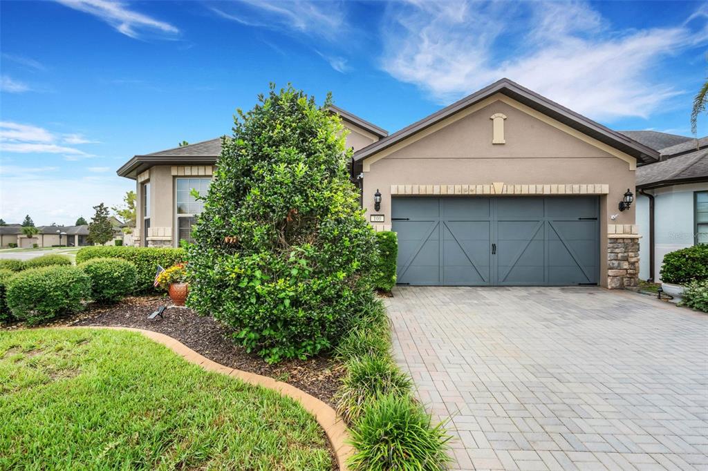 A single-story house exterior features a gray garage door, stone accents, and a landscaped yard — 100 CASTELLON COURT, DAVENPORT, FL
