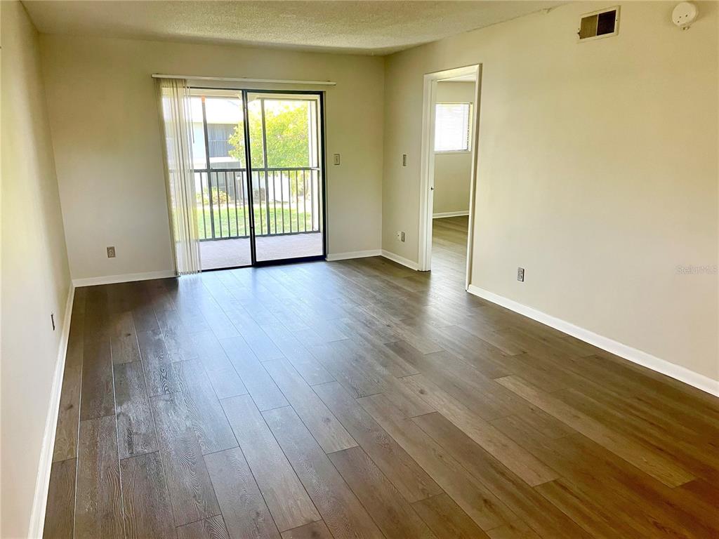 An empty living room features wood-look flooring, beige walls, and a sliding glass door — 6033 34TH STREET W UNIT 104, BRADENTON, FL