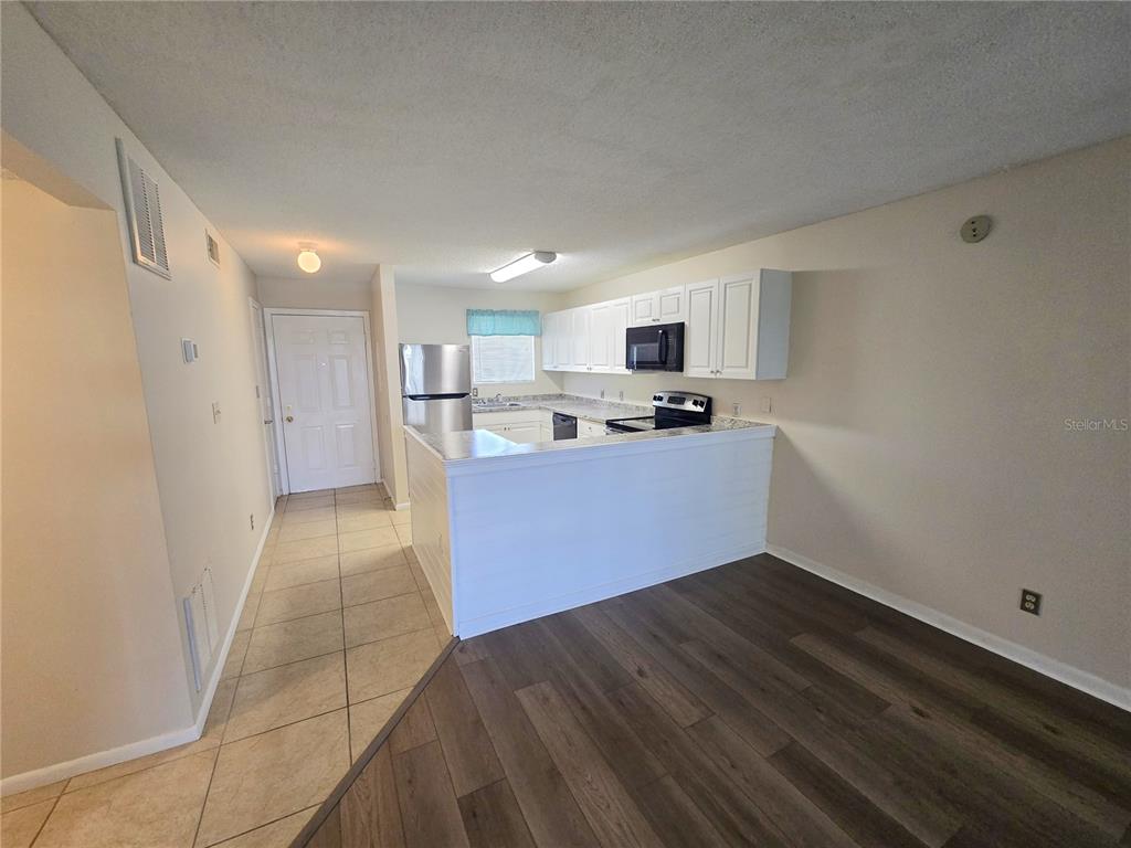 A kitchen with white cabinets, stainless steel appliances, and a breakfast bar overlooks a room — 6033 34TH STREET W UNIT 104, BRADENTON, FL