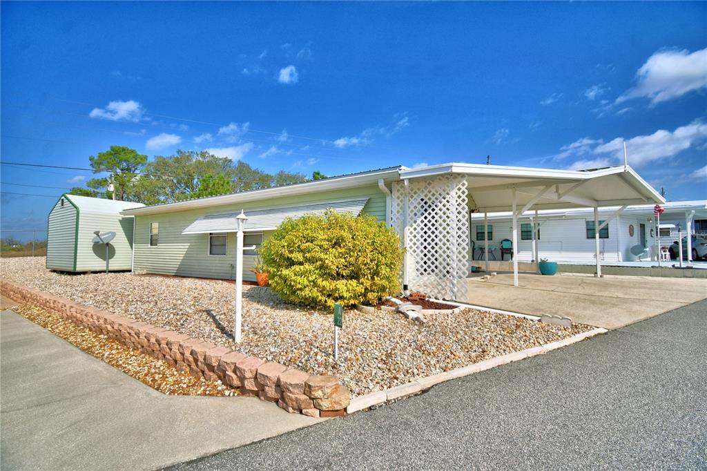 A light green mobile home features a gravel yard, a stone retaining wall, and a carport — 251 PATTERSON ROAD UNIT A22, HAINES CITY, FL