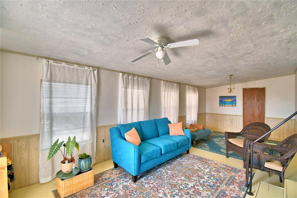 A living room features a blue sofa, wicker chairs, a patterned rug, and wood paneling — 251 PATTERSON ROAD UNIT A22, HAINES CITY, FL