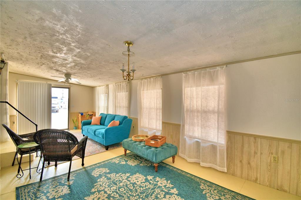 A living room features a blue sofa, a matching ottoman, and wood-paneled lower walls — 251 PATTERSON ROAD UNIT A22, HAINES CITY, FL