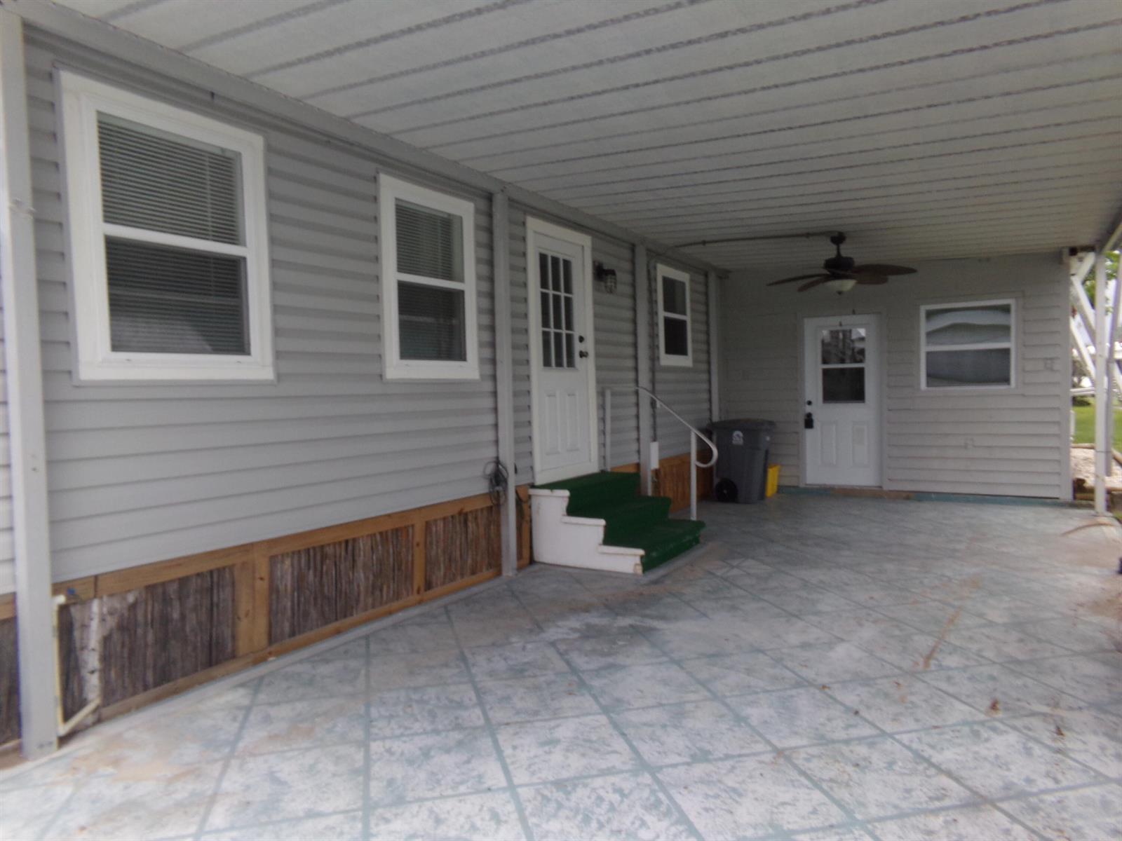 A gray-sided home features a covered carport, concrete patio, and two white entry doors — 59005 Captiva Bay, Boynton Beach FL 33436, BOYNTON BEACH, FL