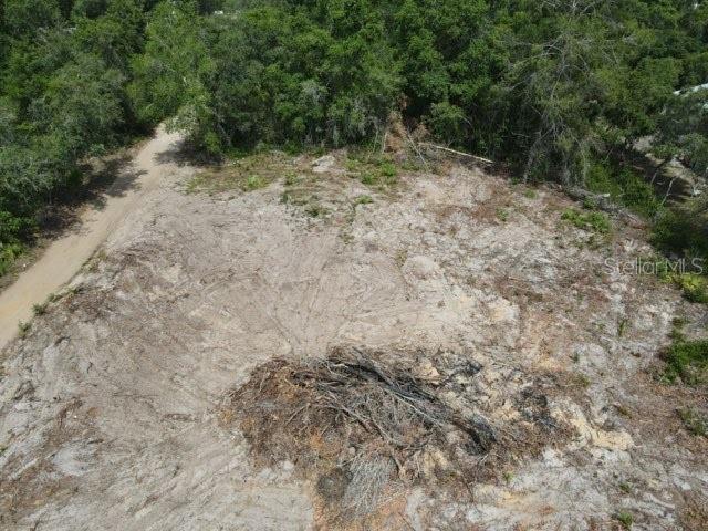 An aerial view shows a cleared, sandy lot bordered by dense trees and a dirt road — X SE 143RD LN, UMATILLA, FL