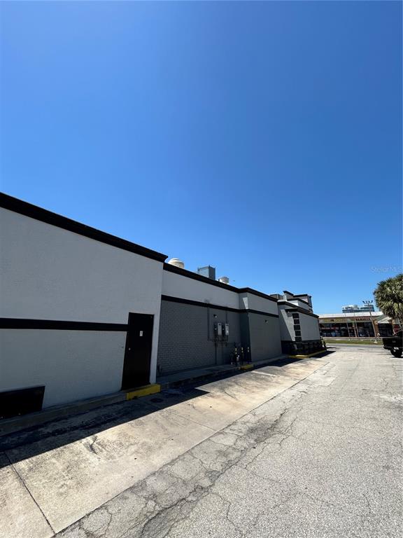 The exterior of a commercial building features a concrete walkway and a dark service door — 6320 INTERNATIONAL DRIVE, ORLANDO, FL