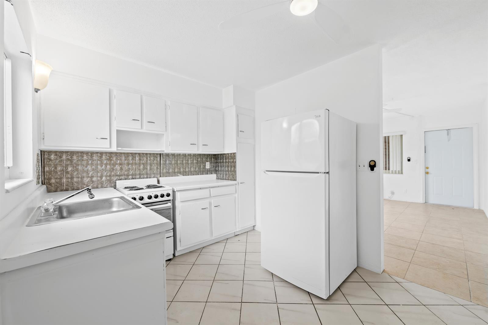 A kitchen with white cabinets, a metal backsplash, and a white refrigerator on tile flooring — 2601 NE 1st Street # 17, Pompano Beach FL 33062, POMPANO BEACH, FL