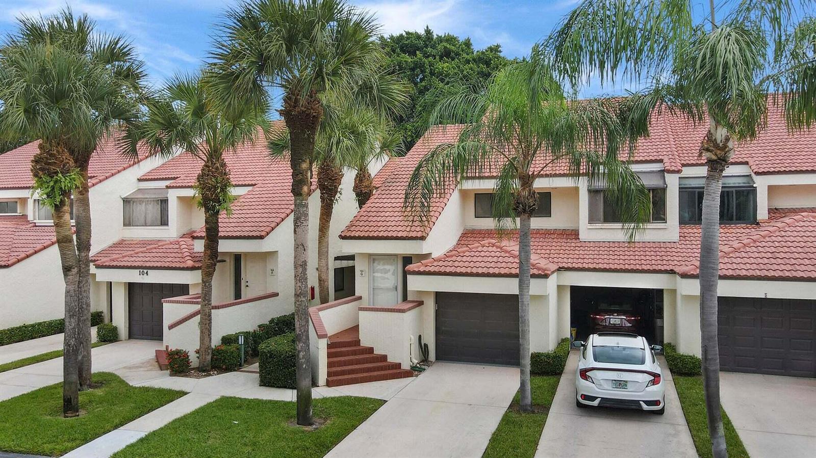An exterior view of two attached townhomes with red tile roofs and palm trees — 104 Sea Oats Drive # G, Juno Beach FL 33408, JUNO BEACH, FL