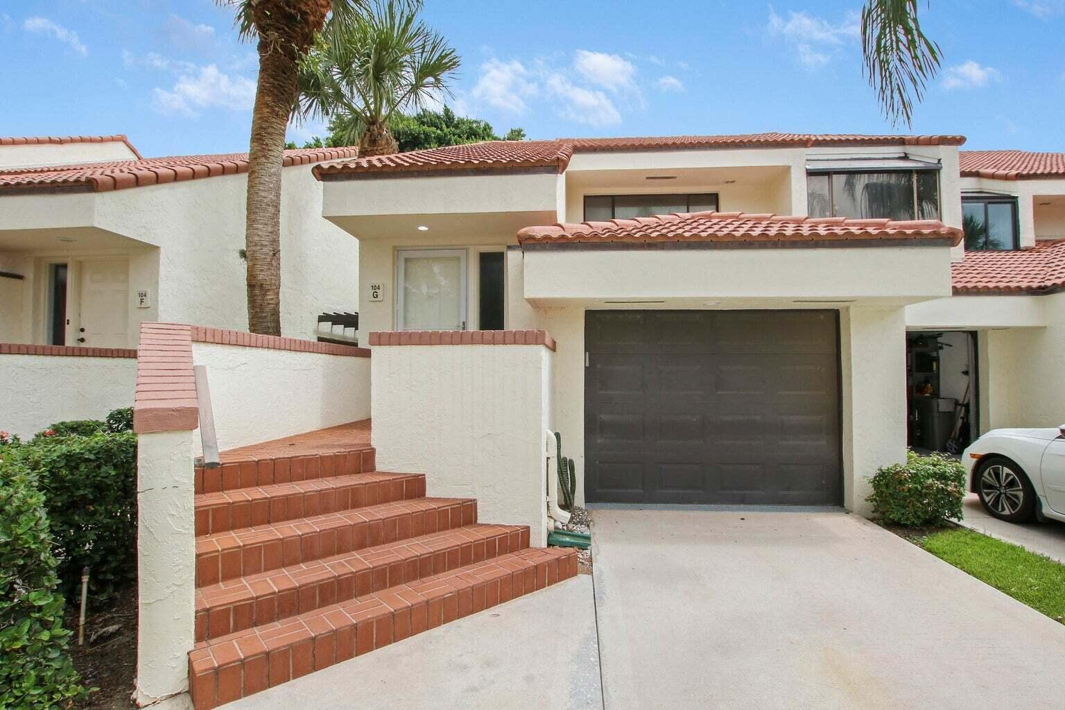 A two-story townhouse exterior features a brown garage door, tiled stairs, and a palm tree — 104 Sea Oats Drive # G, Juno Beach FL 33408, JUNO BEACH, FL