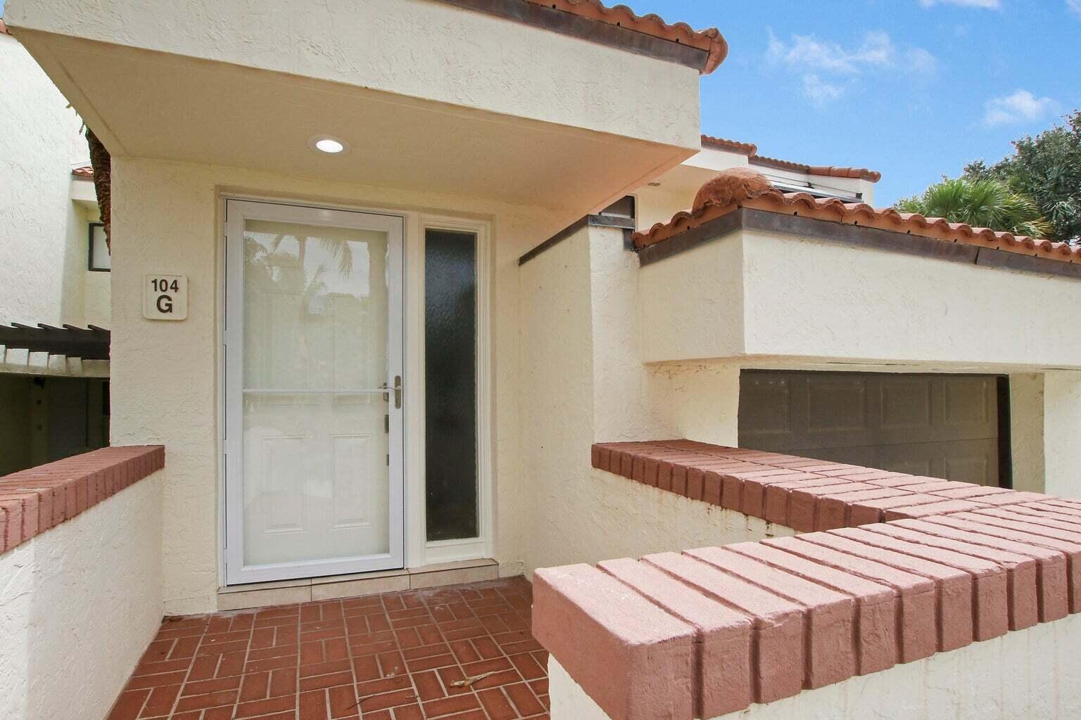 The exterior entrance features a white door, a brick-tiled porch, and a low brick wall — 104 Sea Oats Drive # G, Juno Beach FL 33408, JUNO BEACH, FL