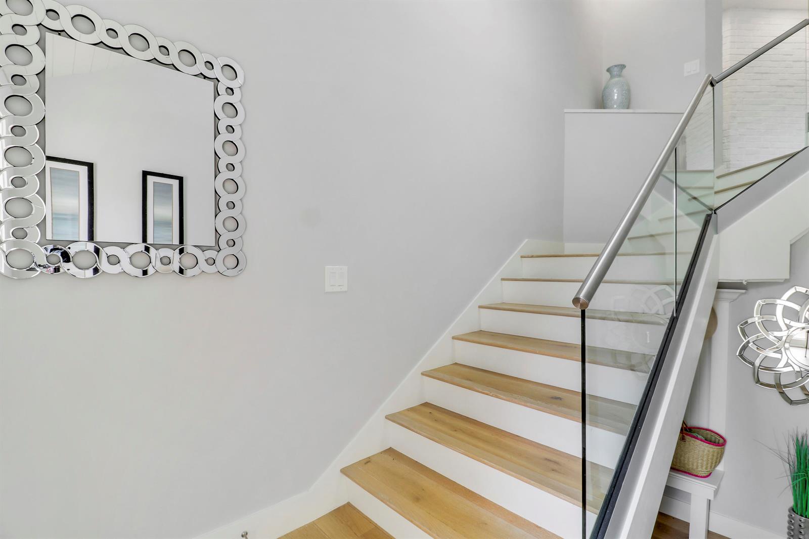 A staircase with light wood treads and a glass railing sits beside a decorative mirror — 104 Sea Oats Drive # G, Juno Beach FL 33408, JUNO BEACH, FL