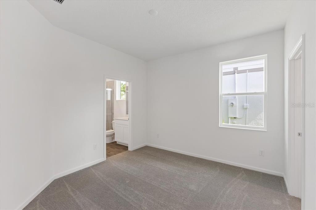 An empty bedroom with white walls, gray carpet, a window, and an attached bathroom — 2257 SIRENA LANE, MOUNT DORA, FL