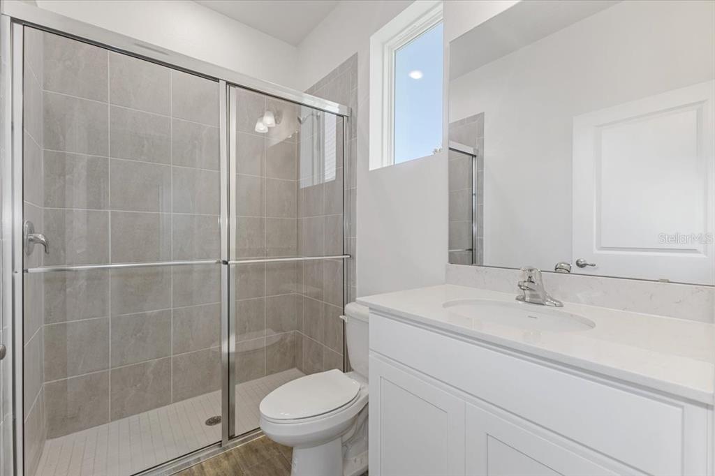 A bathroom features a glass-enclosed tiled shower, a white vanity, and a toilet — 2257 SIRENA LANE, MOUNT DORA, FL