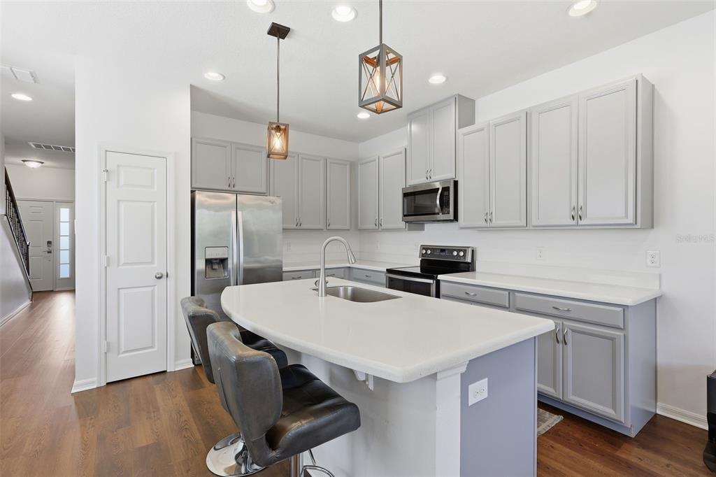 A kitchen features gray cabinets, stainless steel appliances, a curved island, and wood-look flooring — 141 MITCHELL CREEK WAY, OVIEDO, FL