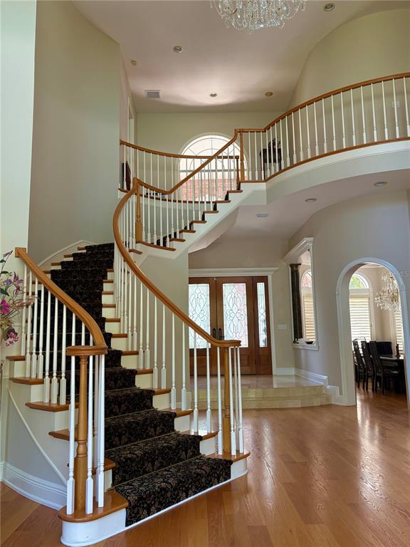 A grand foyer features a curved staircase with dark patterned carpet and a wooden railing — 2817 ROEHAMPTON CLOSE, TARPON SPRINGS, FL