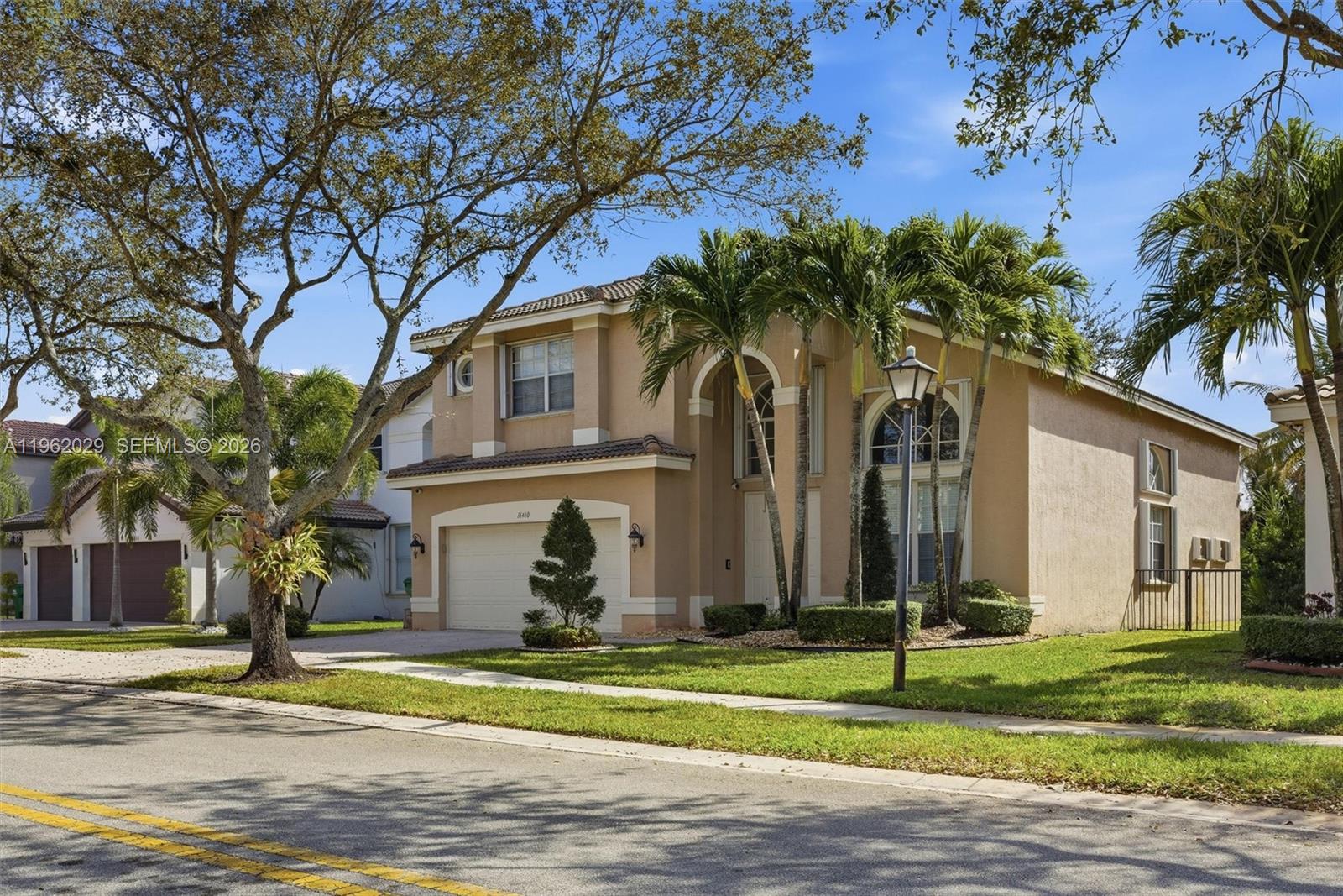 A two-story tan stucco house features a two-car garage, arched windows, and palm trees — 16460 SW 30th Street, Miramar FL 33027, MIRAMAR, FL